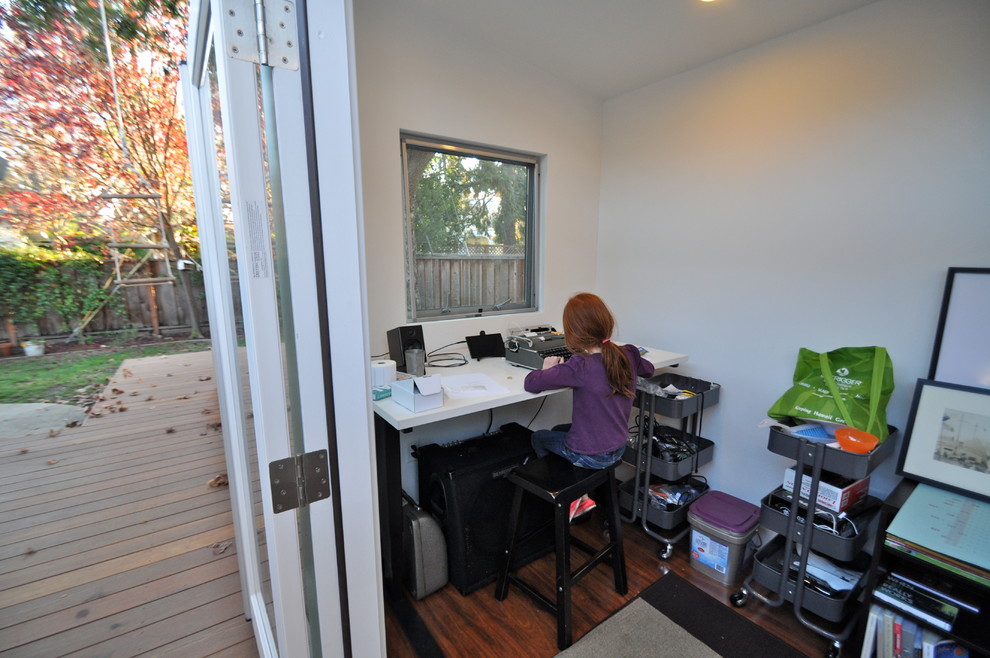 This is an example of a small modern home office in San Francisco with white walls, laminate floors and a freestanding desk.