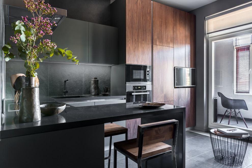 Inspiration for a small contemporary l-shaped open plan kitchen in Saint Petersburg with flat-panel cabinets, grey cabinets, solid surface benchtops, grey splashback, porcelain splashback, stainless steel appliances, porcelain floors, a peninsula, black floor and black benchtop.