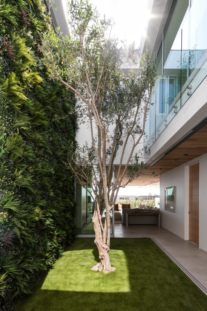 Inspiration pour une terrasse minimaliste de taille moyenne avec une cour, une extension de toiture et un garde-corps en verre.