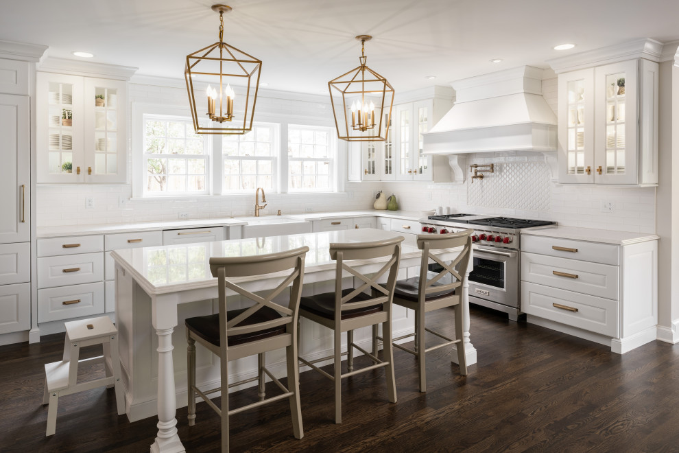 Inspiration for a large traditional l-shaped open plan kitchen in Kansas City with a belfast sink, white cabinets, engineered stone countertops, white splashback, ceramic splashback, integrated appliances, dark hardwood flooring, an island, white worktops and raised-panel cabinets.