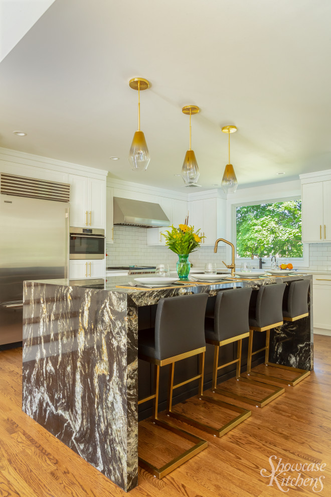 Photo of an expansive contemporary l-shaped kitchen in New York with a farmhouse sink, shaker cabinets, white cabinets, granite benchtops, white splashback, ceramic splashback, stainless steel appliances, light hardwood floors, with island, brown floor and brown benchtop.