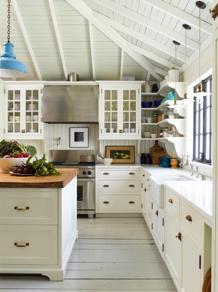 Large country l-shaped kitchen in San Francisco with a farmhouse sink, white cabinets, wood benchtops, white splashback, stainless steel appliances, painted wood floors, with island, glass-front cabinets, white floor, white benchtop and exposed beam.