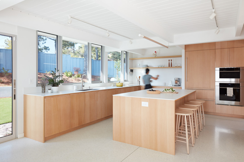 This is an example of a midcentury u-shaped open plan kitchen in San Francisco with an undermount sink, flat-panel cabinets, medium wood cabinets, quartz benchtops, white splashback, engineered quartz splashback, stainless steel appliances, terrazzo floors, with island, white floor, white benchtop and timber.