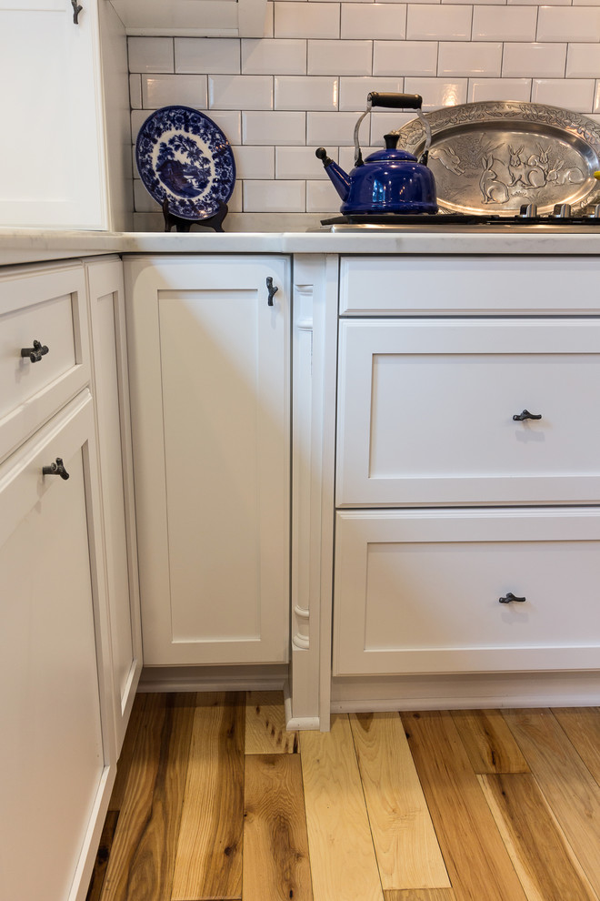 Inspiration for a large transitional u-shaped medium tone wood floor and brown floor enclosed kitchen remodel with an undermount sink, shaker cabinets, white cabinets, quartzite countertops, white backsplash, subway tile backsplash, stainless steel appliances and an island