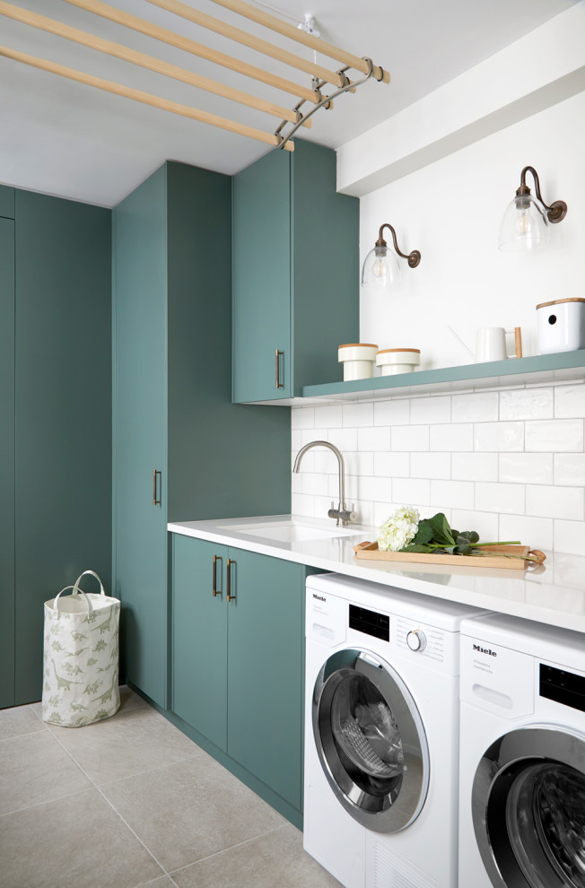 This is an example of a mid-sized contemporary galley utility room in London with an integrated sink, flat-panel cabinets, turquoise cabinets, solid surface benchtops, white splashback, porcelain splashback, white walls, porcelain floors, a side-by-side washer and dryer, beige floor and white benchtop.