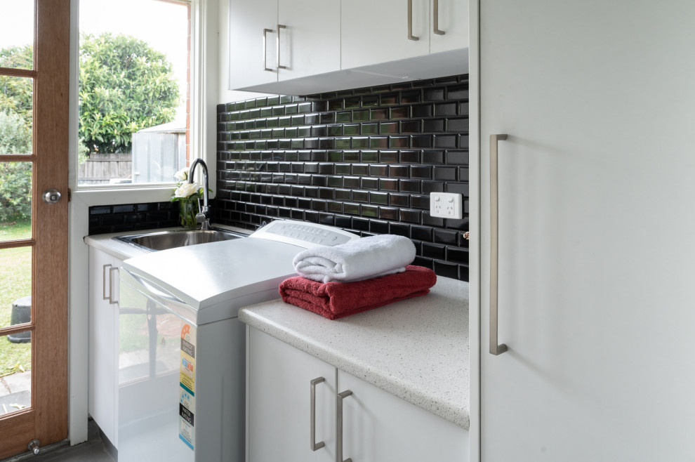 Foto di una lavanderia minimalista con ante bianche, top in laminato, paraspruzzi nero, paraspruzzi con piastrelle a mosaico e top bianco