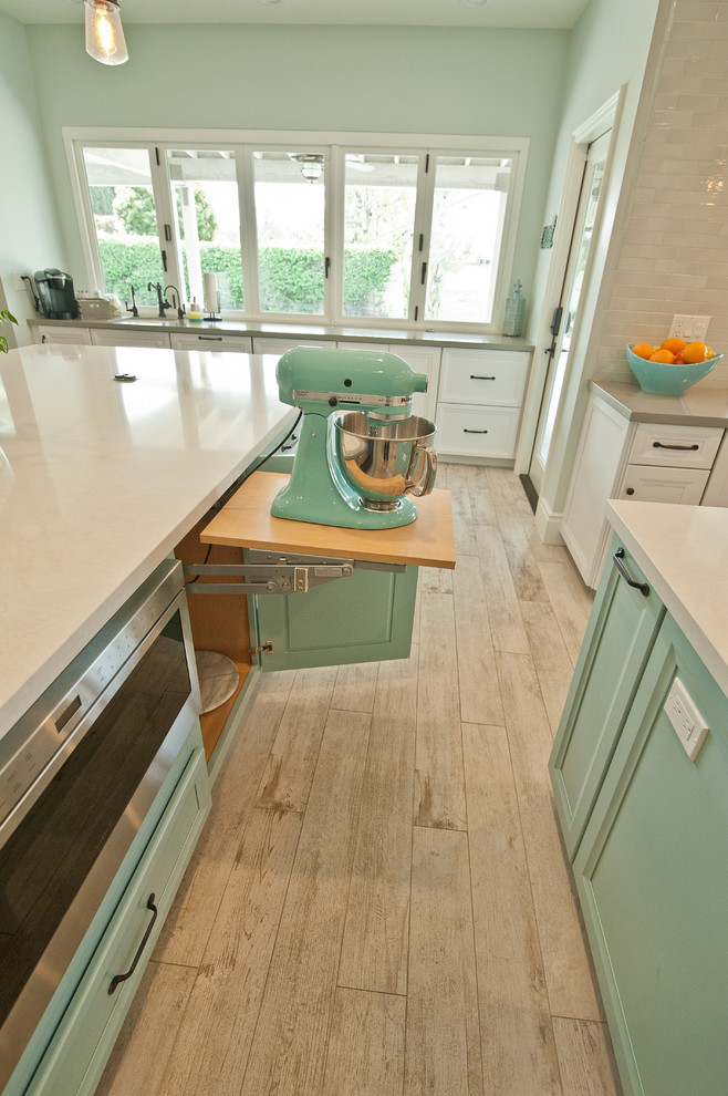 Photo of an expansive beach style u-shaped open plan kitchen in Orange County with a farmhouse sink, raised-panel cabinets, white cabinets, quartz benchtops, blue splashback, ceramic splashback, stainless steel appliances, ceramic floors and multiple islands.