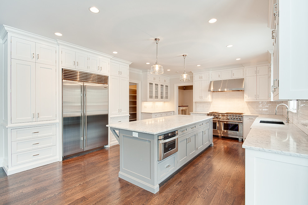 Eat-in kitchen - large transitional u-shaped dark wood floor and brown floor eat-in kitchen idea with an undermount sink, shaker cabinets, white cabinets, white backsplash, stainless steel appliances and an island