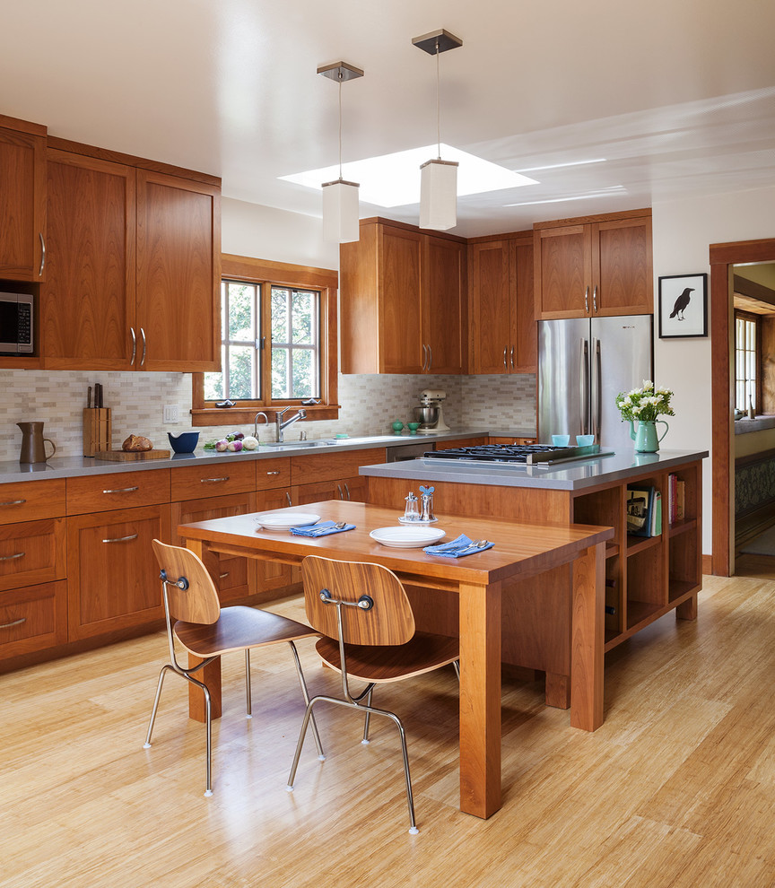This is an example of a mid-sized arts and crafts l-shaped eat-in kitchen in San Francisco with shaker cabinets, medium wood cabinets, stainless steel appliances, with island, quartz benchtops, beige splashback, ceramic splashback, bamboo floors and beige floor.