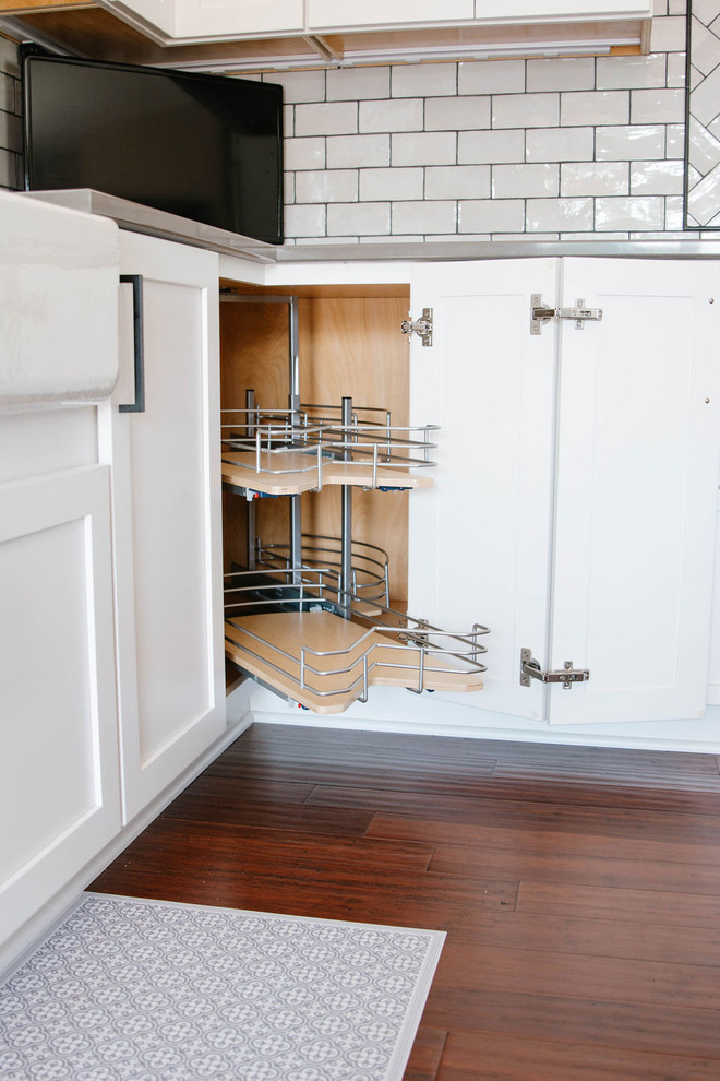 Inspiration for a mid-sized transitional l-shaped medium tone wood floor and brown floor eat-in kitchen remodel in Omaha with a farmhouse sink, shaker cabinets, white cabinets, quartzite countertops, white backsplash, subway tile backsplash, stainless steel appliances, an island and white countertops