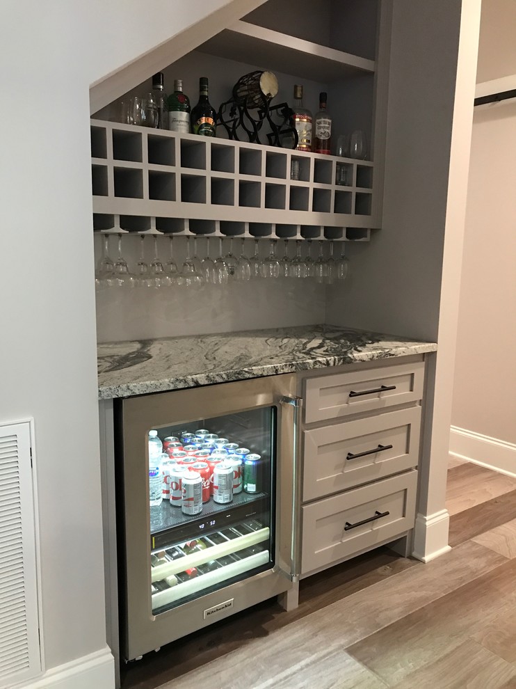 Design ideas for a small arts and crafts single-wall home bar in Raleigh with shaker cabinets, grey cabinets, granite benchtops, grey splashback, light hardwood floors and grey floor.