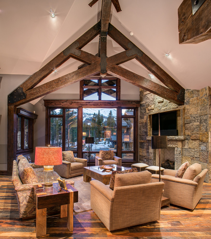 Photo of a country open concept living room in Denver with dark hardwood floors, a standard fireplace, a stone fireplace surround and a wall-mounted tv.
