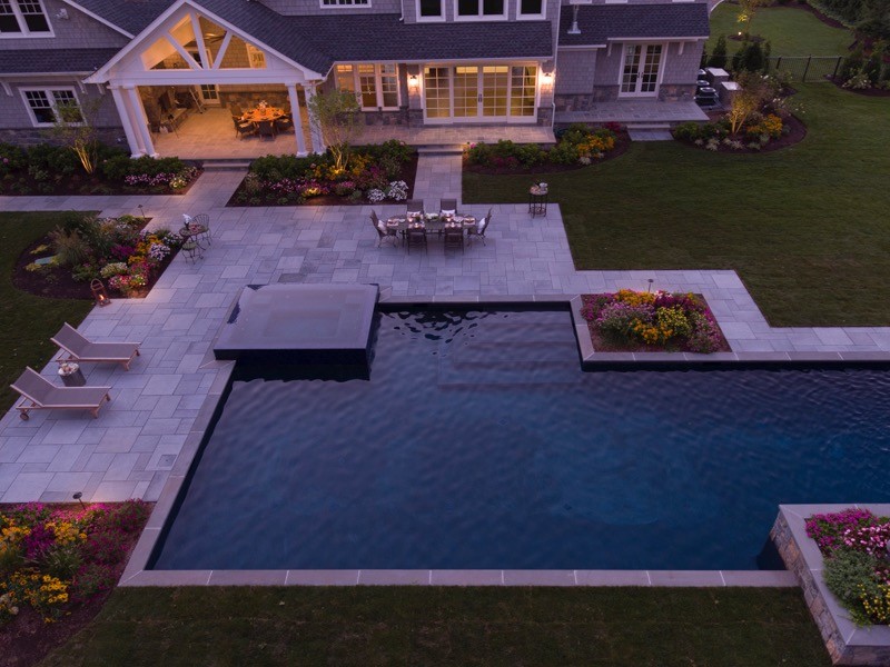This is an example of an expansive contemporary backyard rectangular lap pool in New York with a hot tub and natural stone pavers.
