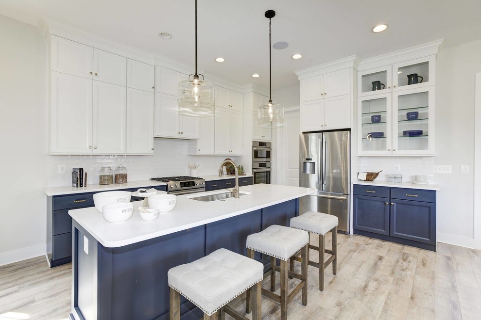 Transitional kitchen in DC Metro with an undermount sink, recessed-panel cabinets, blue cabinets, white splashback, subway tile splashback, stainless steel appliances, with island, beige floor and white benchtop.