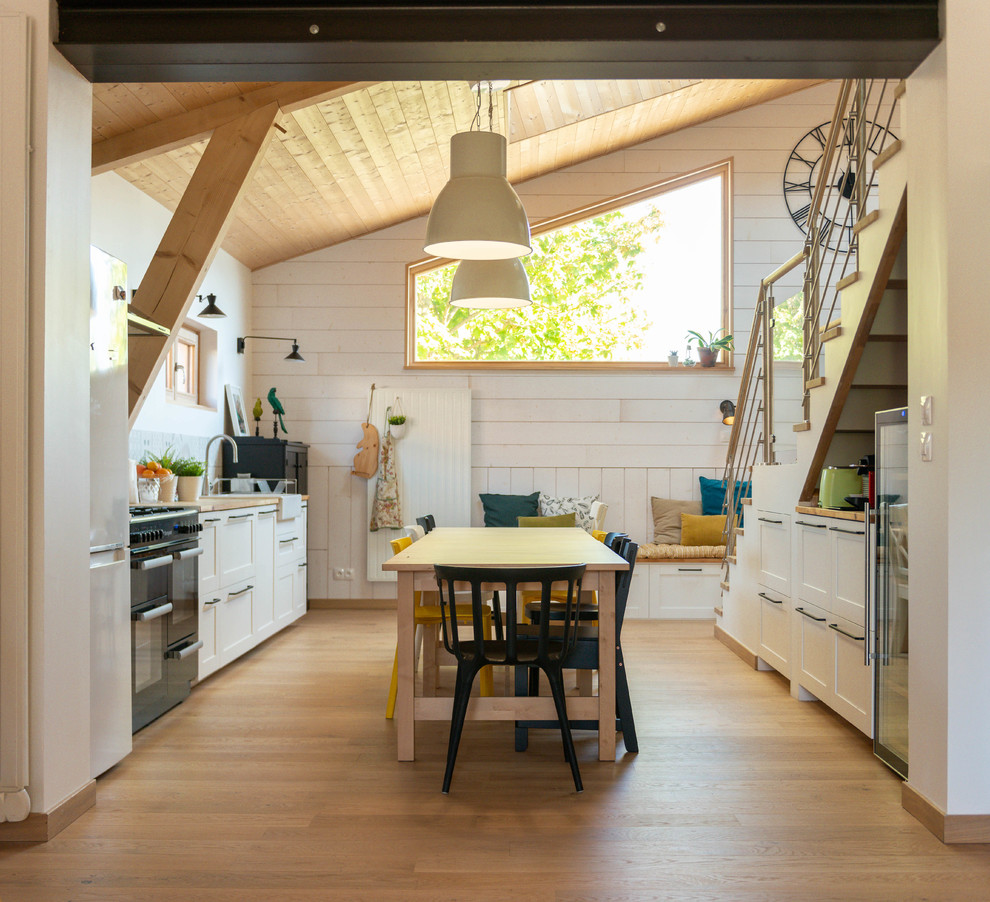 Design ideas for an expansive scandinavian kitchen in Grenoble with a farmhouse sink, shaker cabinets, white cabinets, wood benchtops, black appliances, light hardwood floors, beige floor and beige benchtop.