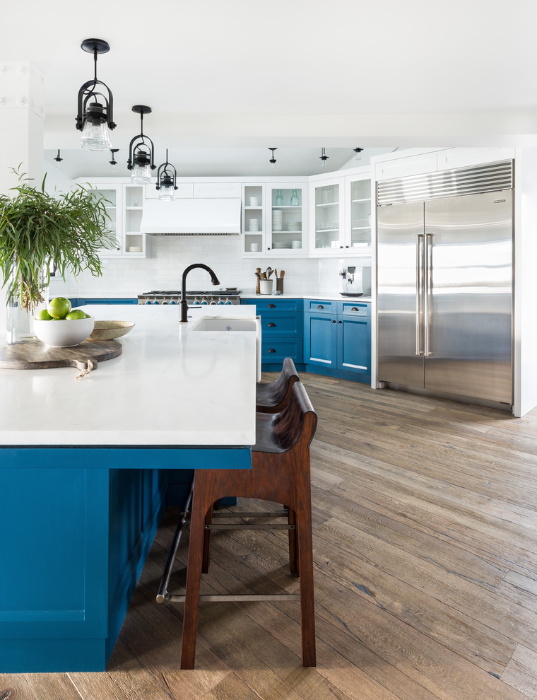 Design ideas for a beach style galley open plan kitchen in Seattle with a farmhouse sink, glass-front cabinets, white cabinets, stainless steel appliances, light hardwood floors and with island.