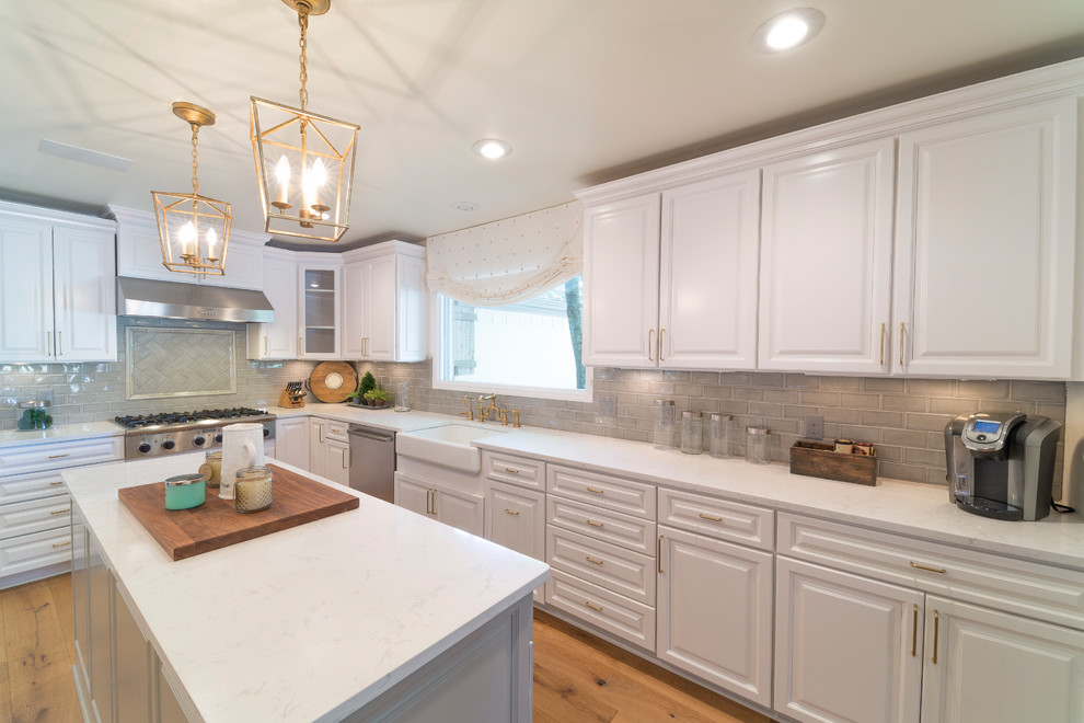 Enclosed kitchen - large transitional u-shaped medium tone wood floor and brown floor enclosed kitchen idea with a farmhouse sink, raised-panel cabinets, white cabinets, quartz countertops, gray backsplash, glass tile backsplash, stainless steel appliances and an island