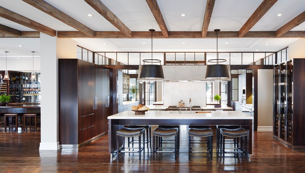 This is an example of a large country l-shaped eat-in kitchen in Chicago with a double-bowl sink, flat-panel cabinets, dark wood cabinets, solid surface benchtops, stainless steel appliances, medium hardwood floors, with island and brown floor.