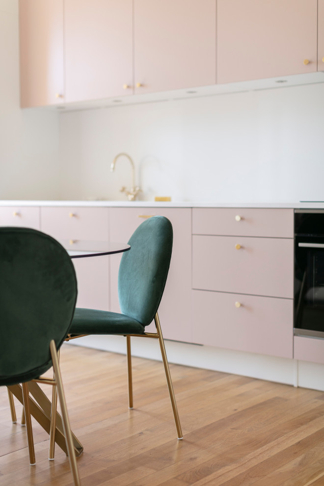 Photo of a mid-sized contemporary single-wall open plan kitchen in Nice with an undermount sink, pink cabinets, quartzite benchtops, white splashback, engineered quartz splashback, black appliances, light hardwood floors, white benchtop, recessed, beaded inset cabinets, no island and brown floor.