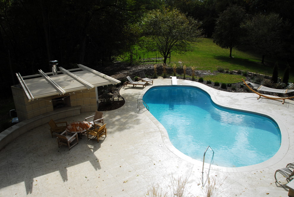 Mid-sized contemporary backyard kidney-shaped pool in Cedar Rapids with a pool house and stamped concrete.