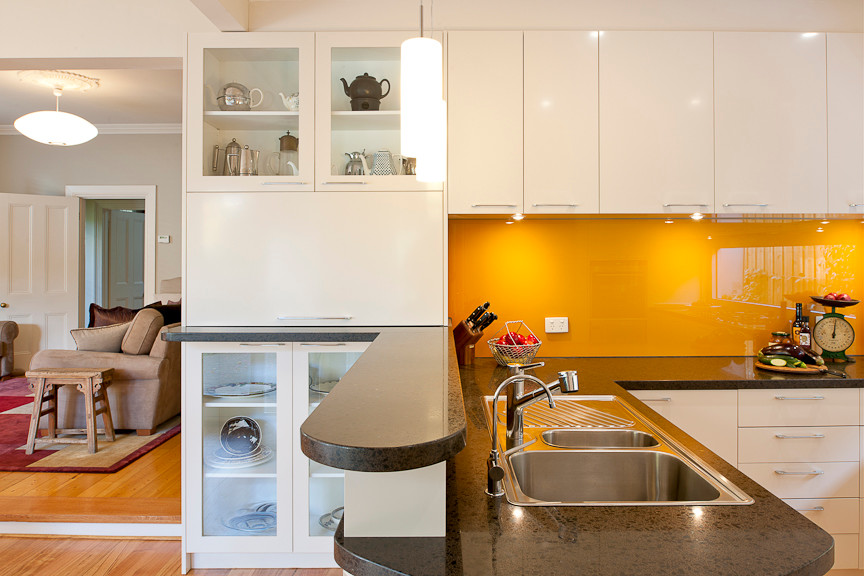 Photo of a mid-sized traditional galley eat-in kitchen in Melbourne with a peninsula, flat-panel cabinets, white cabinets, quartz benchtops, orange splashback, glass sheet splashback, stainless steel appliances, a double-bowl sink and light hardwood floors.
