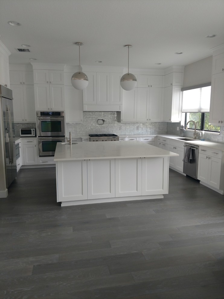 Inspiration for a large transitional u-shaped dark wood floor and gray floor enclosed kitchen remodel in Miami with an undermount sink, shaker cabinets, white cabinets, quartz countertops, white backsplash, stainless steel appliances, an island and white countertops