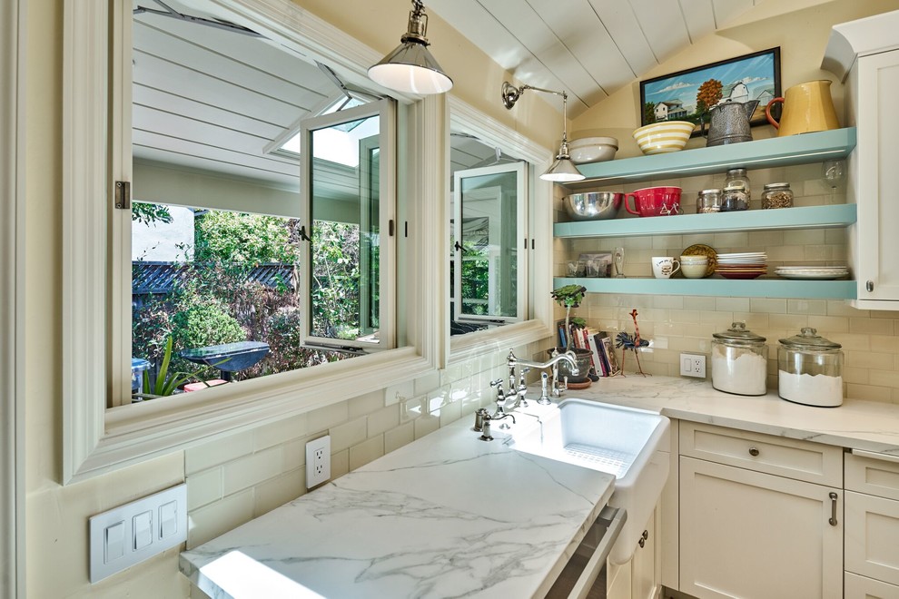 Photo of a mid-sized country l-shaped eat-in kitchen in San Francisco with a farmhouse sink, shaker cabinets, yellow cabinets, marble benchtops, white splashback, glass tile splashback, stainless steel appliances, ceramic floors and a peninsula.
