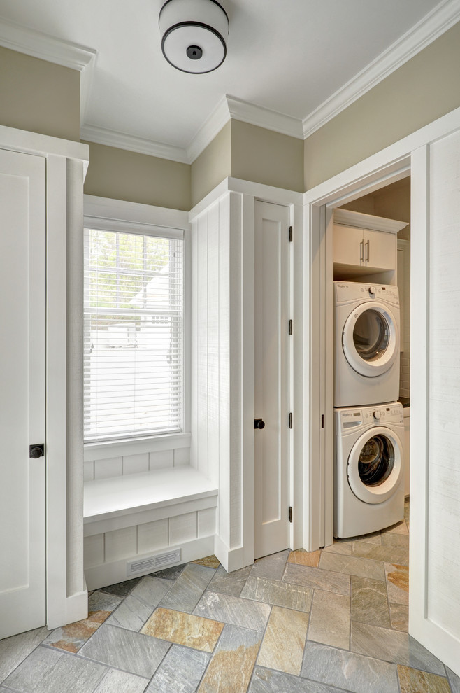 Mid-sized traditional laundry room in New York with flat-panel cabinets, white cabinets, beige walls, travertine floors and a stacked washer and dryer.