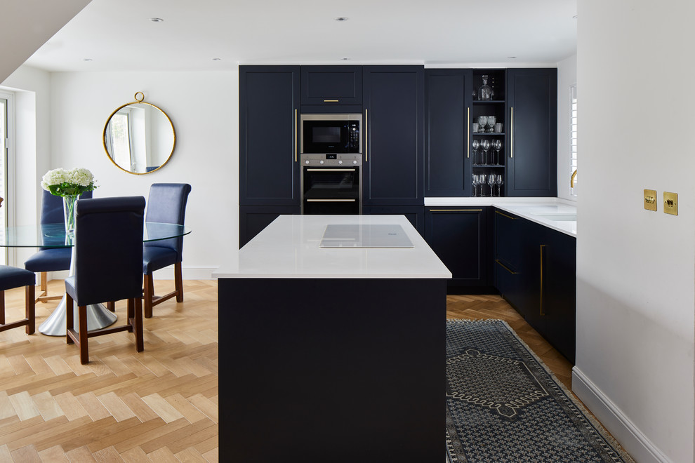 Inspiration for a mid-sized transitional l-shaped eat-in kitchen in London with shaker cabinets, blue cabinets, quartzite benchtops, stainless steel appliances, with island, white benchtop, a single-bowl sink and light hardwood floors.