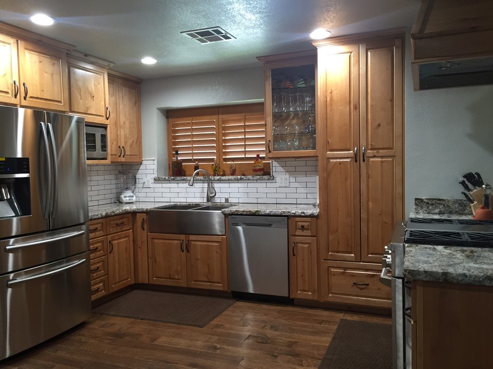 Mid-sized mountain style u-shaped medium tone wood floor kitchen photo with an undermount sink, raised-panel cabinets, light wood cabinets, granite countertops, white backsplash, ceramic backsplash and stainless steel appliances