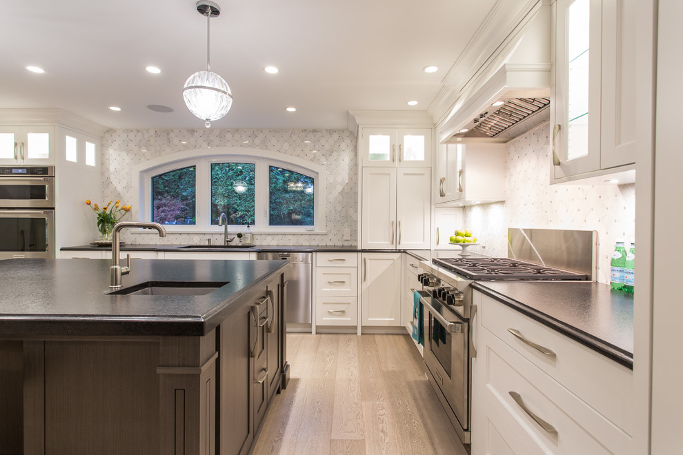 Large transitional l-shaped eat-in kitchen in Vancouver with an undermount sink, shaker cabinets, white cabinets, granite benchtops, grey splashback, marble splashback, stainless steel appliances, medium hardwood floors, with island, beige floor and black benchtop.