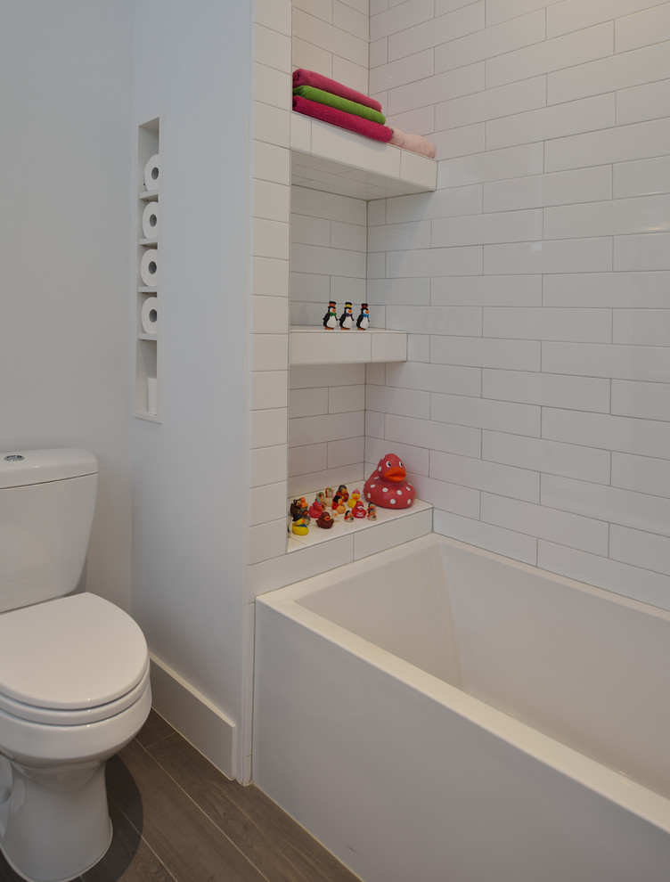 Inspiration for a mid-sized modern kids bathroom in Houston with flat-panel cabinets, white cabinets, an alcove tub, a shower/bathtub combo, a two-piece toilet, white tile, ceramic tile, white walls, porcelain floors, an undermount sink, solid surface benchtops, brown floor and a shower curtain.