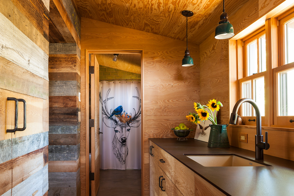 Mid-sized mountain style galley concrete floor enclosed kitchen photo with an undermount sink, flat-panel cabinets, medium tone wood cabinets, wood backsplash, no island and black countertops