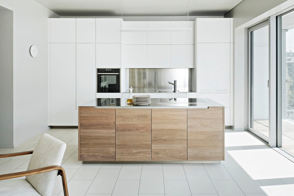 This is an example of a mid-sized contemporary single-wall open plan kitchen in Milan with flat-panel cabinets, white cabinets, stainless steel benchtops, metallic splashback, black appliances, with island and white floor.