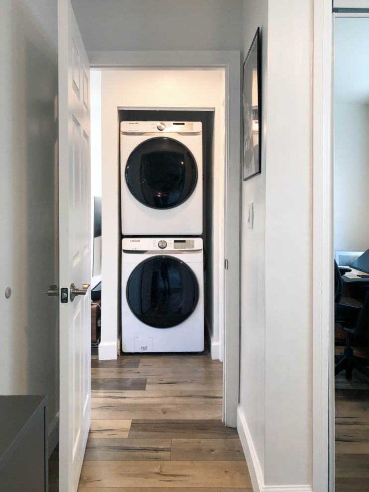 Photo of a small scandinavian galley laundry cupboard in Los Angeles with a stacked washer and dryer, brown floor, flat-panel cabinets, white cabinets, white benchtop, granite benchtops, beige walls, laminate floors and a drop-in sink.