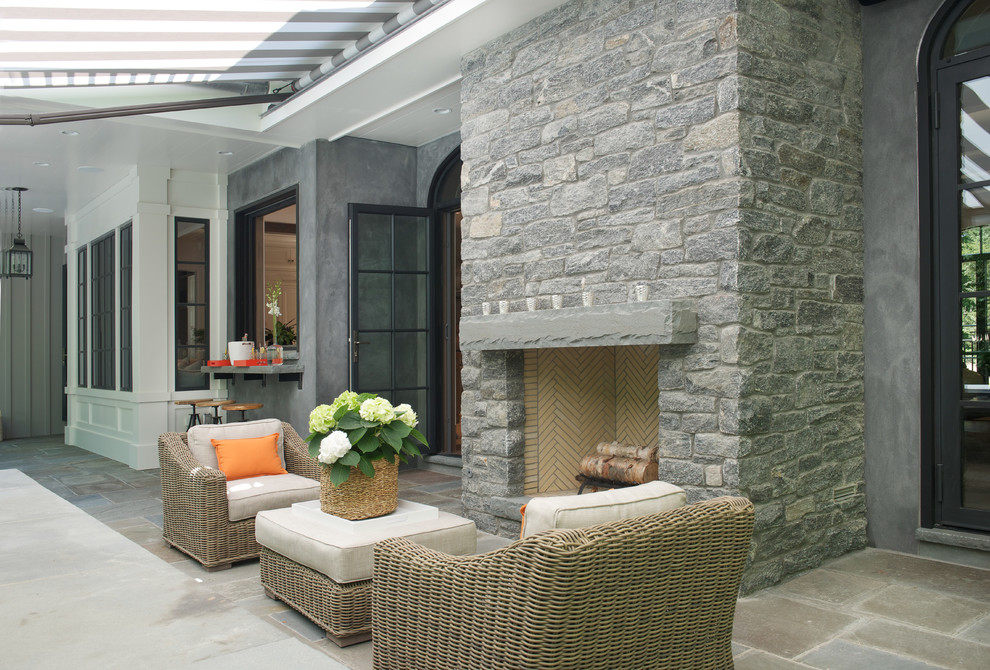 Photo of a large transitional backyard verandah in New York with natural stone pavers, a fire feature and an awning.