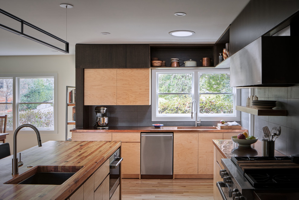 This is an example of a mid-sized midcentury u-shaped eat-in kitchen in Atlanta with a farmhouse sink, flat-panel cabinets, light wood cabinets, copper benchtops, grey splashback, stainless steel appliances, light hardwood floors, a peninsula, brown floor and brown benchtop.