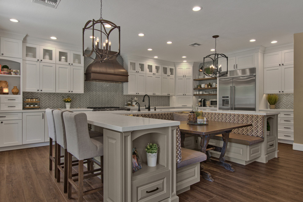 Example of a large transitional u-shaped vinyl floor and brown floor eat-in kitchen design with recessed-panel cabinets, white cabinets, quartz countertops, gray backsplash, ceramic backsplash, stainless steel appliances, an island and white countertops