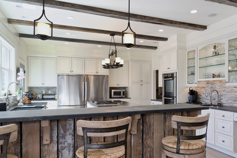 Transitional u-shaped open concept kitchen photo with a farmhouse sink, raised-panel cabinets, white cabinets, soapstone countertops, multicolored backsplash and stainless steel appliances