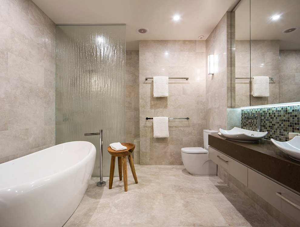 This is an example of a contemporary bathroom in Melbourne with a vessel sink, flat-panel cabinets, grey cabinets, a freestanding tub, a curbless shower, a two-piece toilet, mosaic tile, beige walls and beige tile.