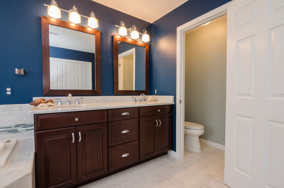 This is an example of a large transitional master bathroom in DC Metro with an undermount sink, raised-panel cabinets, medium wood cabinets, granite benchtops, a drop-in tub, a corner shower, a two-piece toilet, white tile, porcelain tile, blue walls and porcelain floors.