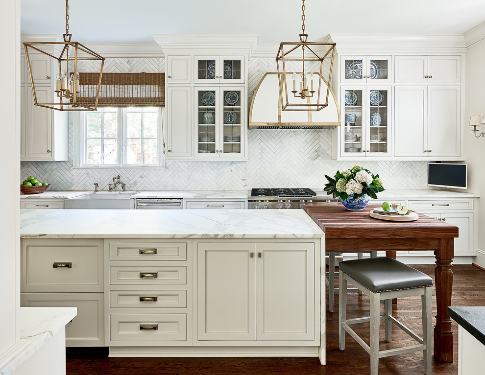Example of a large classic dark wood floor kitchen design in Charlotte with a farmhouse sink, marble countertops, stone tile backsplash, stainless steel appliances, white cabinets, glass-front cabinets, white backsplash and two islands