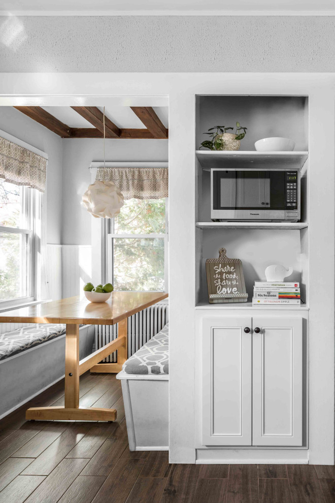 Example of a mid-sized farmhouse l-shaped porcelain tile and brown floor eat-in kitchen design in Philadelphia with a single-bowl sink, flat-panel cabinets, white cabinets, quartzite countertops, white backsplash, ceramic backsplash, stainless steel appliances and gray countertops