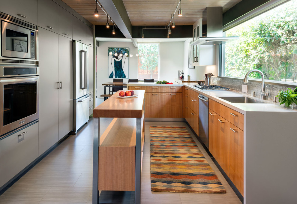 Photo of a large contemporary eat-in kitchen in San Francisco with a single-bowl sink, flat-panel cabinets, stainless steel appliances, with island, light wood cabinets, solid surface benchtops, grey splashback, mosaic tile splashback, laminate floors and brown floor.