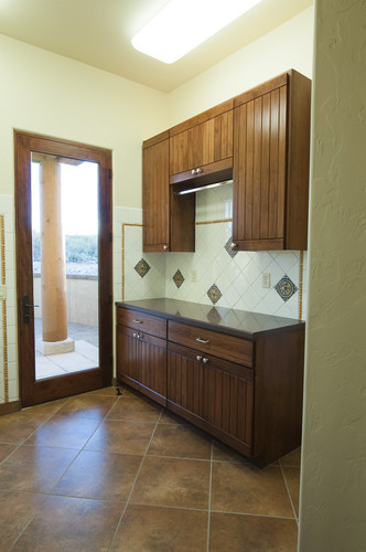 This is an example of a mid-sized eclectic galley dedicated laundry room in Phoenix with an undermount sink, dark wood cabinets, quartz benchtops, ceramic floors and a stacked washer and dryer.