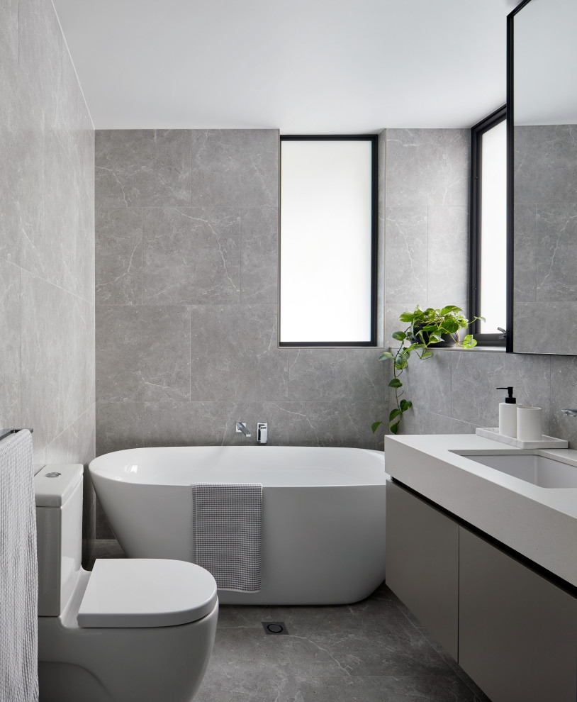 Inspiration for a mid-sized contemporary master bathroom with grey cabinets, a curbless shower, gray tile, porcelain tile, porcelain floors, an undermount sink, engineered quartz benchtops, grey floor, a hinged shower door and white benchtops.