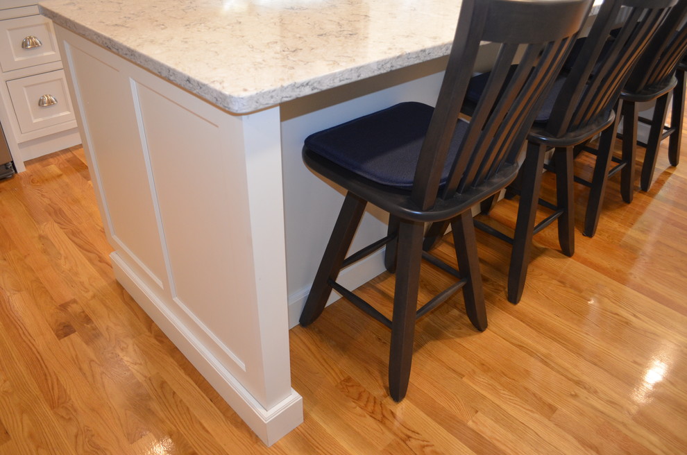 Example of a transitional l-shaped light wood floor eat-in kitchen design in Boston with an undermount sink, beaded inset cabinets, white cabinets, quartz countertops, white backsplash, ceramic backsplash, stainless steel appliances, an island and gray countertops