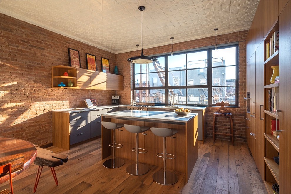 Photo of a large industrial l-shaped eat-in kitchen in New York with a single-bowl sink, flat-panel cabinets, medium wood cabinets, window splashback, medium hardwood floors and with island.