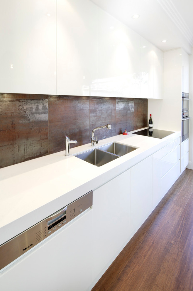 This is an example of a large contemporary galley open plan kitchen in Sydney with with island, an undermount sink, flat-panel cabinets, white cabinets, quartz benchtops, metallic splashback, stainless steel appliances, brown floor, white benchtop, porcelain splashback and medium hardwood floors.