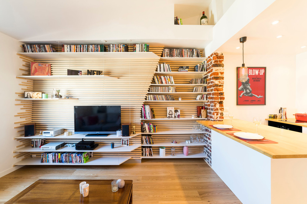 This is an example of a small contemporary open concept family room in Paris with a library, white walls, light hardwood floors, no fireplace, a freestanding tv and brown floor.